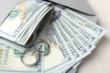 İki gümüş alyans, bir dolarlık banknotlar ve beyaz masanın üzerindeki zarf, yakın plan.