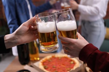 Arkadaşlar masada bira bardaklarını tokuşturur, yakın plan