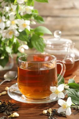Aromatik yasemin çayı cam bardakta, çaydanlık, demlik ve çiçekler ahşap masada, yakın plan.