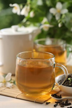 Lezzetli yasemin çayı fincanlar, çaydanlık, kuru yapraklar ve çiçekler beyaz ahşap masada, yakın plan.