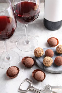 Açık gri arka planda lezzetli trüf şekerleri ve kırmızı şarap, yakın plan.