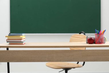 Farklı okul kırtasiyesi ve kırmızı elma, kapalı alanda tahtaya yakın ahşap masada.