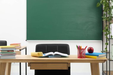 Farklı okul kırtasiyesi ve kırmızı elma, kapalı alanda tahtaya yakın ahşap masada.