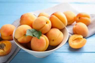 Açık mavi ahşap masada yeşil yapraklı taze kayısılar, yakın plan.