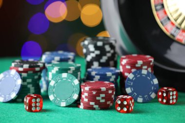 Kumarhane fişleri, zarlar ve rulet tekerleği yeşil masada bulanık ışıklara karşı, yakın plan