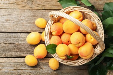 Hasır sepetin içinde taze kayısılar ve ahşap masanın üzerinde yeşil yapraklar. Metin için boşluk