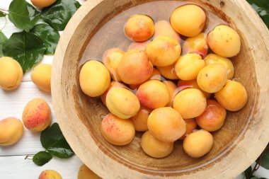 Taze kayısılar kasede su ve yeşil yapraklarla bembeyaz ahşap masada, düz yatıyordu.