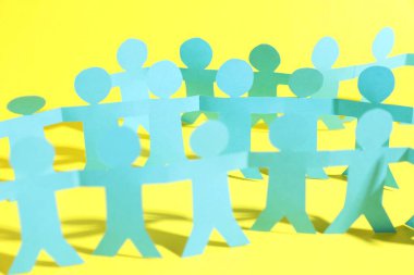 Sarı arka planda el ele tutuşan insan kağıt figürleri, yakın plan