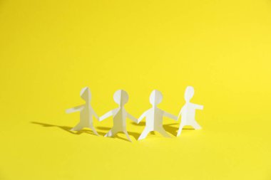 Sarı arka planda el ele tutuşan insan kağıt figürleri