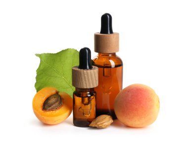 Beyaz üzerine izole edilmiş yağ şişeleri, taze kayısılar, çekirdekler ve yeşil yaprak.