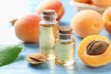 Yağ şişeleri, taze kayısılar ve çekirdekler açık mavi ahşap masa, yakın plan.