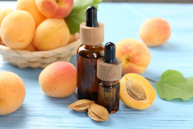 Yağ şişeleri, taze kayısılar ve çekirdekler açık mavi ahşap masa, yakın plan.