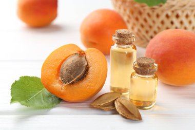 Beyaz ahşap masa üzerinde gerekli yağ şişeleri, taze kayısılar ve çekirdekler, yakın plan.