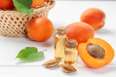 Beyaz ahşap masa üzerinde gerekli yağ şişeleri, taze kayısılar ve çekirdekler, yakın plan.