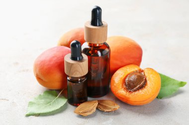 Açık gri masada gerekli yağ şişeleri, taze kayısılar, çekirdekler ve yeşil yapraklar, yakın plan.