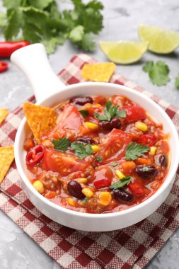 Lezzetli biberli makarna kasede ve gri desenli masada nachos, yakın plan.