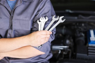 Otomobil parçaları. Kaputu açık, kapalı kaputun yanında anahtarı olan profesyonel bir tamirci, yakın plan. Metin için boşluk