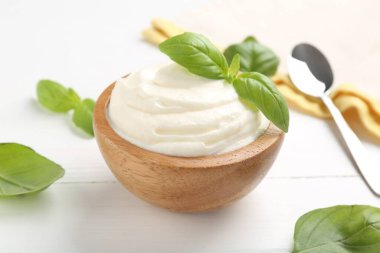 Lezzetli yoğurt, fesleğen ve kaşık beyaz ahşap masada, yakın plan.