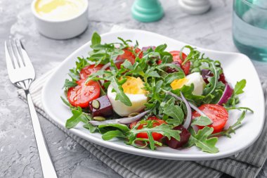 Lezzetli salata roka, sebze ve yumurta gri masada servis edilir, yakın plan.