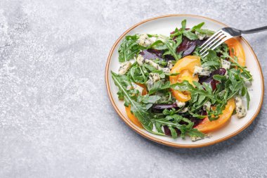 Lezzetli salata roka, mavi peynir ve sebzeler gri desenli masada. Metin için boşluk
