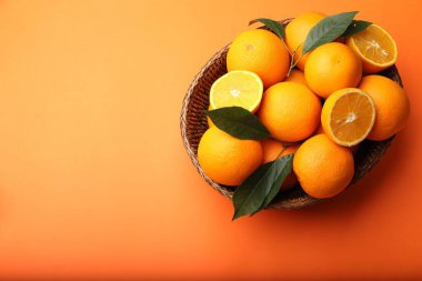Turuncu arka planda taze portakallar ve sepette yeşil yapraklar. Metin için boşluk