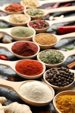 Siyah masadaki kaşıklardaki farklı baharatlar, yakın plan.