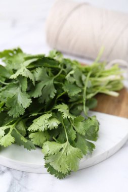 Taze aromatik kişniş, beyaz mermer masa üzerindeki kesme tahtası ve iplik, yakın plan.