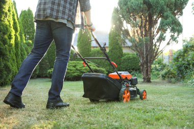 Bahçede çim biçme makinesiyle çimen biçen adam, yakın plan.