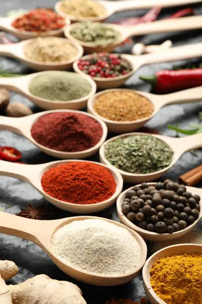 Siyah masadaki kaşıklardaki farklı baharatlar, yakın plan.