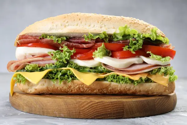 Jambonlu, peynirli ve sebzeli baget sandviç. Gri dokulu masa, yakın plan.