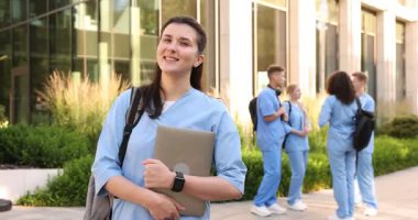 Açık hava binasının yakınında sırt çantası ve dizüstü bilgisayarı olan mutlu tıp öğrencisi, seçici odaklı.