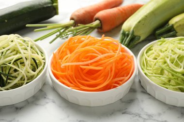 Farklı vejetaryen erişteleri ve beyaz mermer masada taze sebzeler, yakın plan.