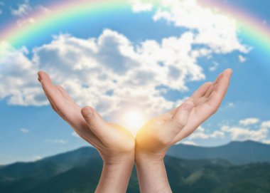 Umut. Gökyüzüne karşı gökkuşağı ve dağlarda güneş ile el ele tutuşan adam, yakın çekim.