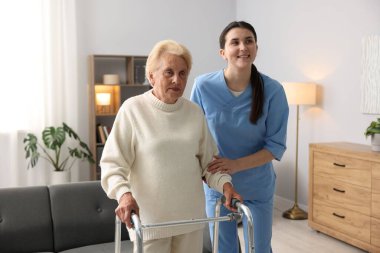 Hemşire içeride yürüyen çerçeveli yaşlı bir kadına yardım ediyor. Ev sağlık hizmetleri