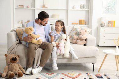 Baba ve kızı evdeki kanepede pelüş hayvanlarla oynuyorlar.