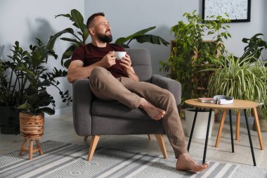 Uyum. Evdeki koltukta içki içen adam.