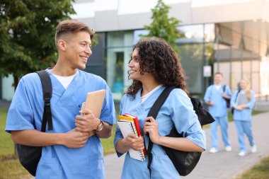 Sırt çantalı ve defterli tıp öğrencileri açık havada, seçici bir odak noktası.