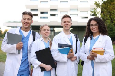 Sırt çantalı ve defterli tıp öğrencileri açık havada, seçici bir odak noktası.