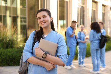 Açık hava binasının yakınında sırt çantası ve dizüstü bilgisayarı olan mutlu tıp öğrencisi, seçici odaklı.