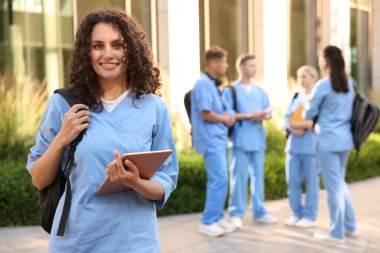 Açık hava binasının yanında sırt çantası ve tabletli mutlu tıp öğrencisi, seçici odaklı.