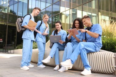 Üniformalı bir grup tıp öğrencisi açık hava binasının yakınında birlikte okuyorlar.