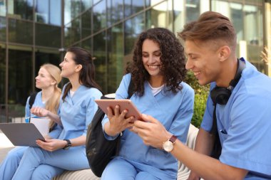 Üniformalı bir grup tıp öğrencisi açık hava binasının yakınında birlikte okuyorlar.