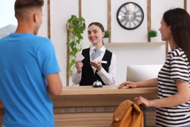 Üniformalı gülen resepsiyonist otel odasındaki resepsiyondaki iki turiste anahtar kartını veriyor.