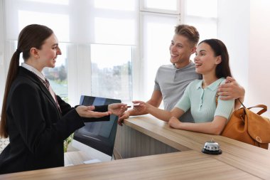 Üniformalı gülen resepsiyonist otel odasındaki resepsiyondaki iki turiste anahtar kartını veriyor.