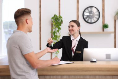 Üniformalı gülen resepsiyonist otel resepsiyonundaki müşteriye misafir odasının anahtarını veriyor.