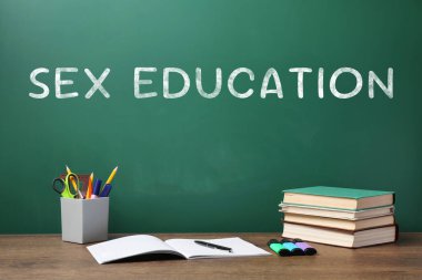 Yeşil karatahta ve ahşap masa üzerindeki kırtasiye malzemelerinde cinsel eğitim yazıları var.