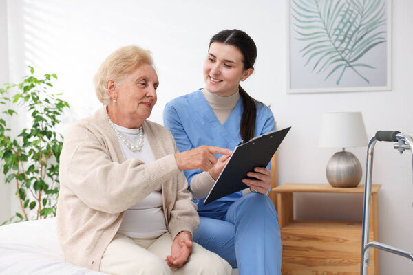 Nurse with clipboard examining senior woman indoors. Home health care service