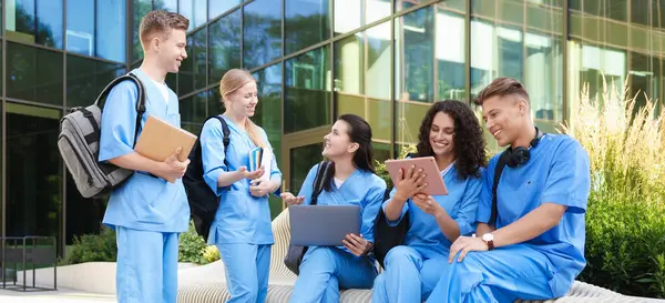 Üniformalı bir grup tıp öğrencisi açık hava binasının yakınında birlikte okuyorlar.