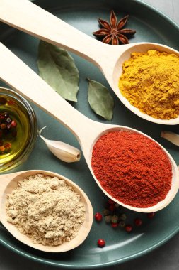 Gri masadaki kaşıklardaki farklı baharatlar, yakın plan.