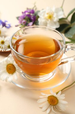 Cam fincanda aromatik bitki çayı ve bej arka planda farklı çiçekler, yakın plan.